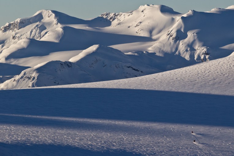 Helen Schettini and Clint Allan riding across the Pemberton Glacier on snowmobiles.